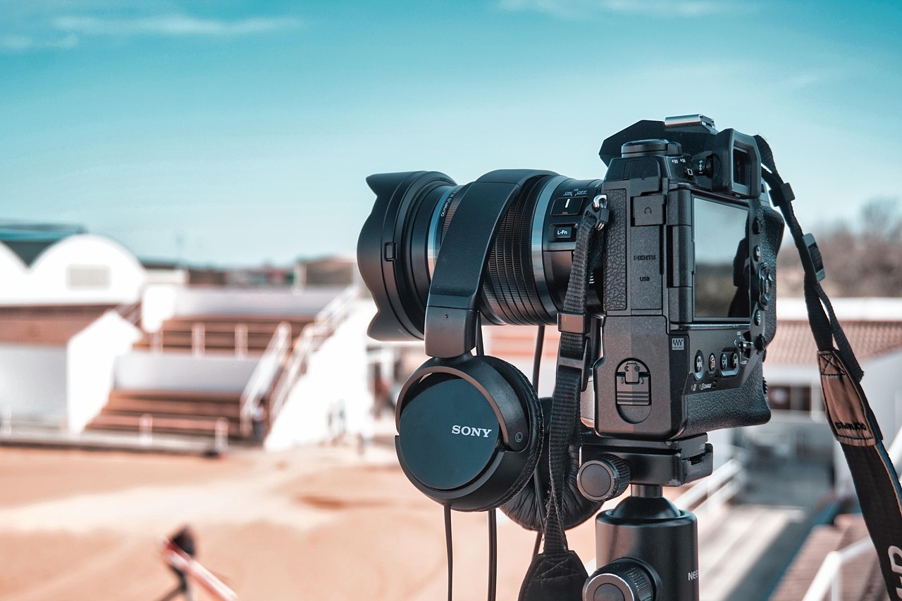 Video camera mounted on a tripod with monitoring headphones at an outdoor filming location